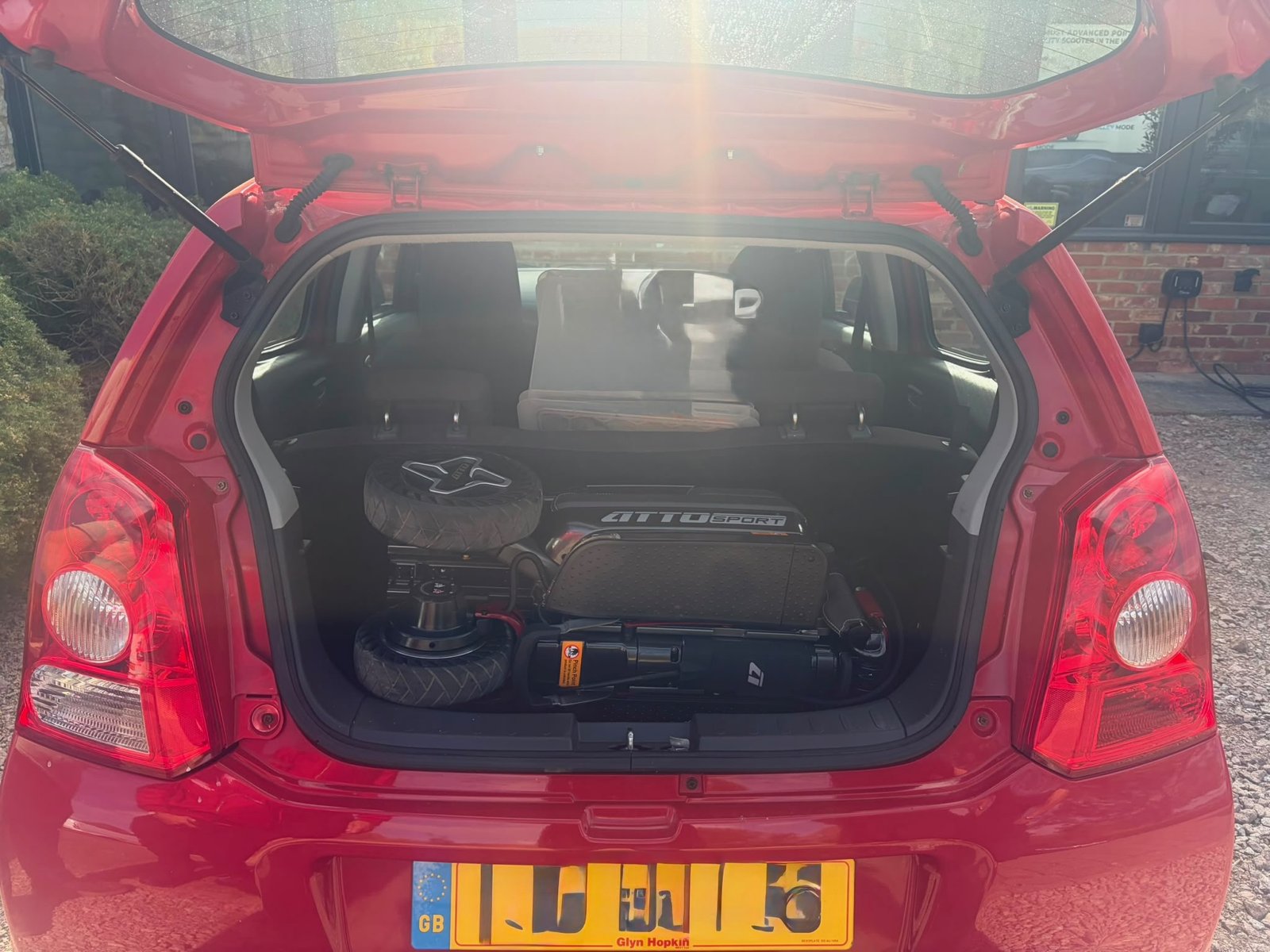 Folded ATTO Sport folding mobility scooter in the boot of a red Suzuki Alto city car